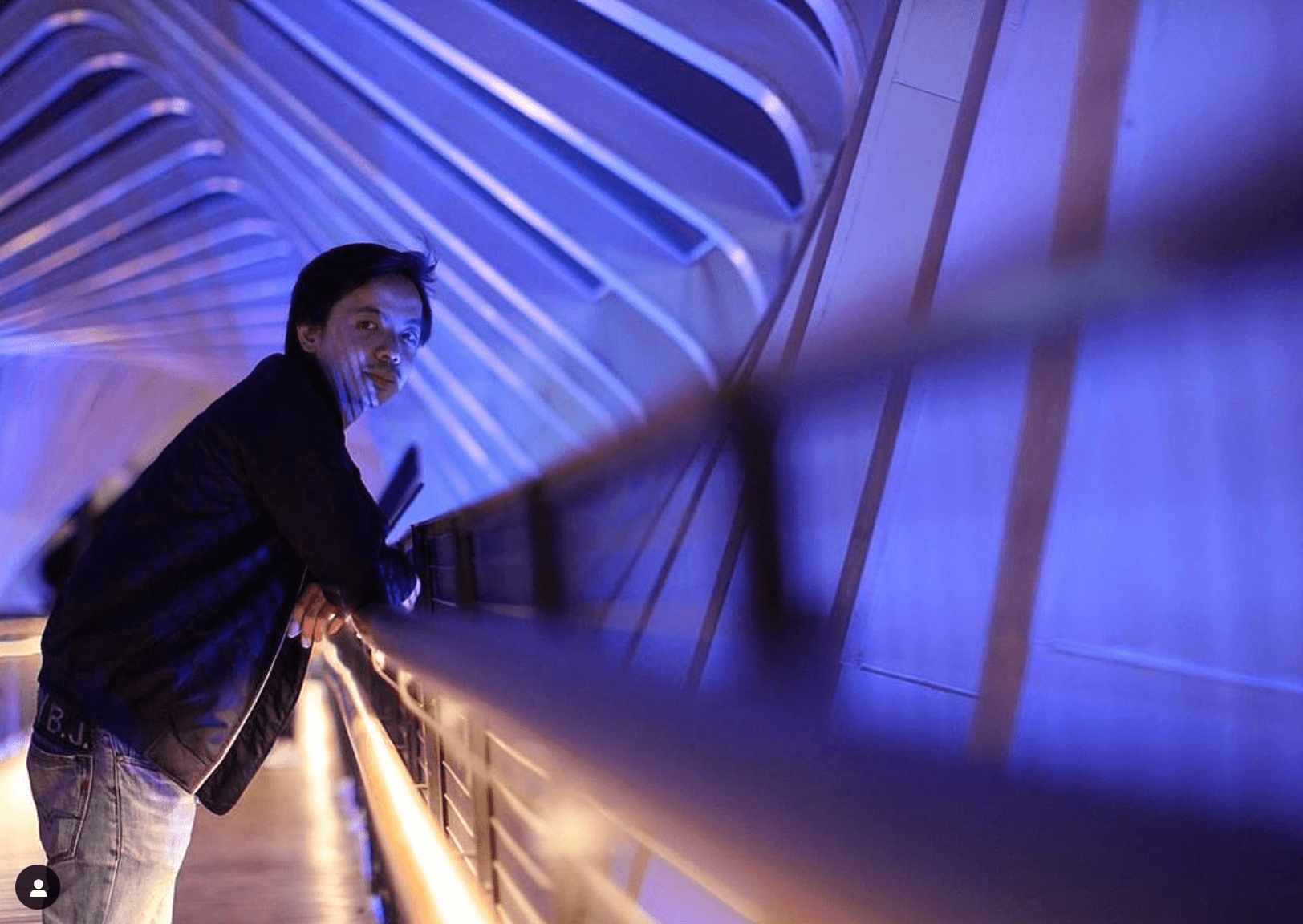 Kevin Septian leaning on a railing at night, lit in blue and violet