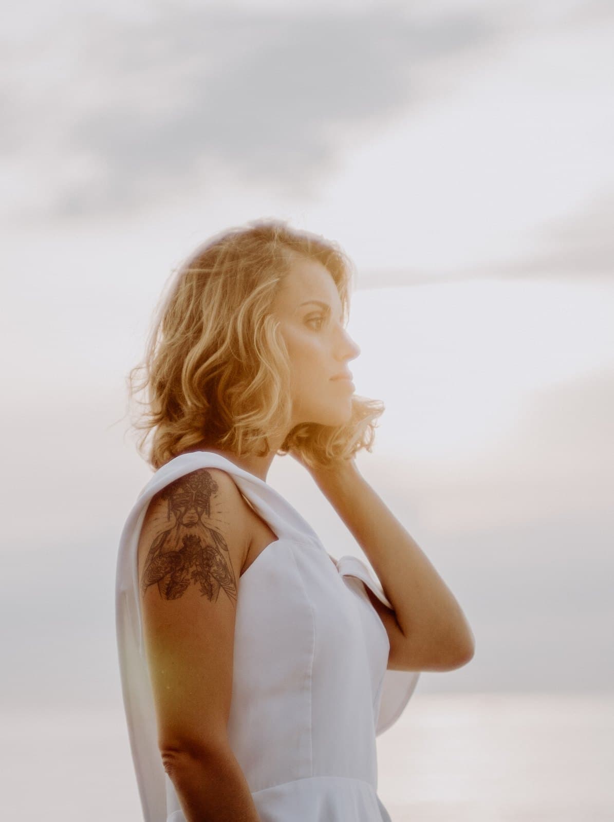 A woman in a white dress by the sea at dusk, looking down