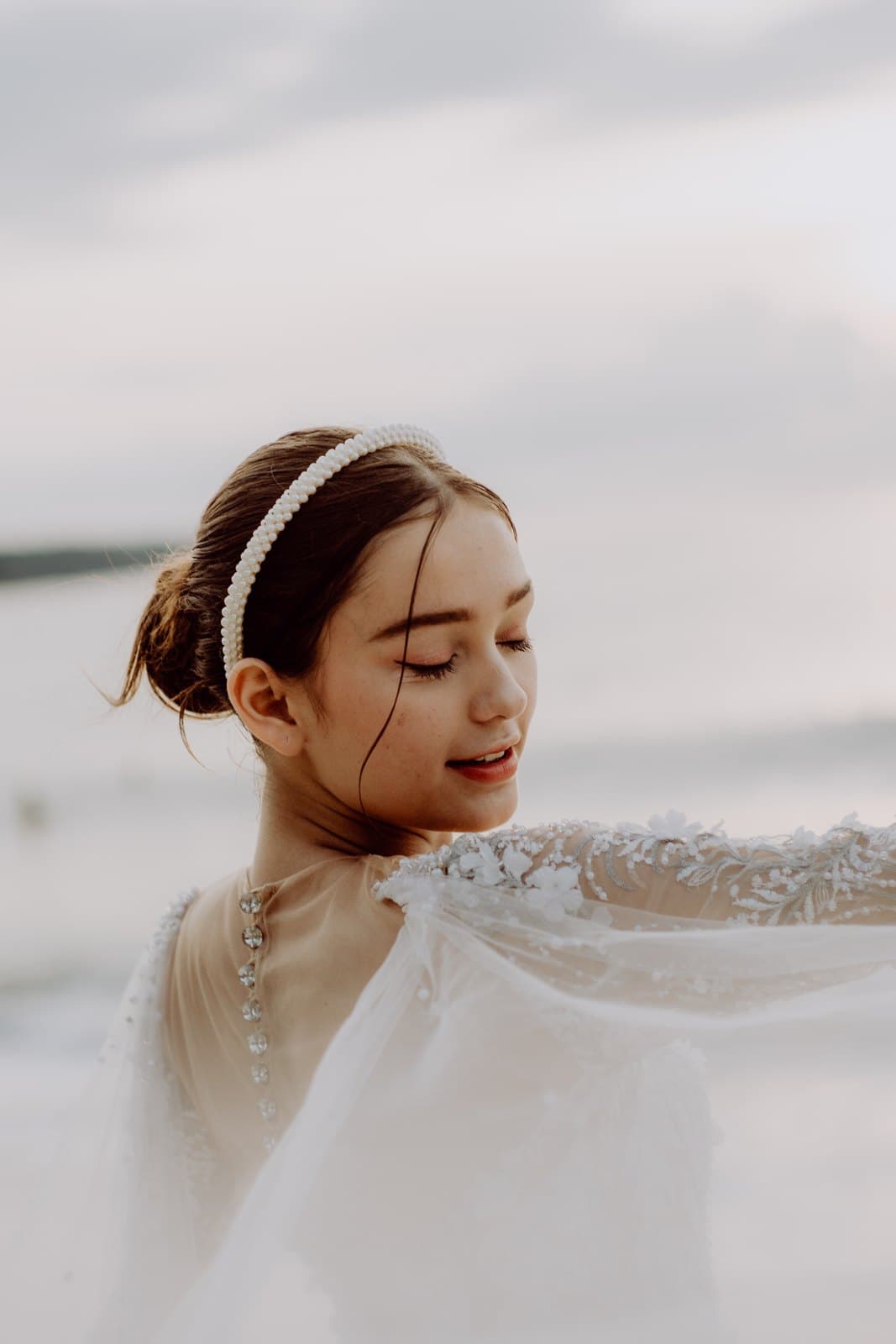 A bride in a lace veil and a pearl headband by the sea