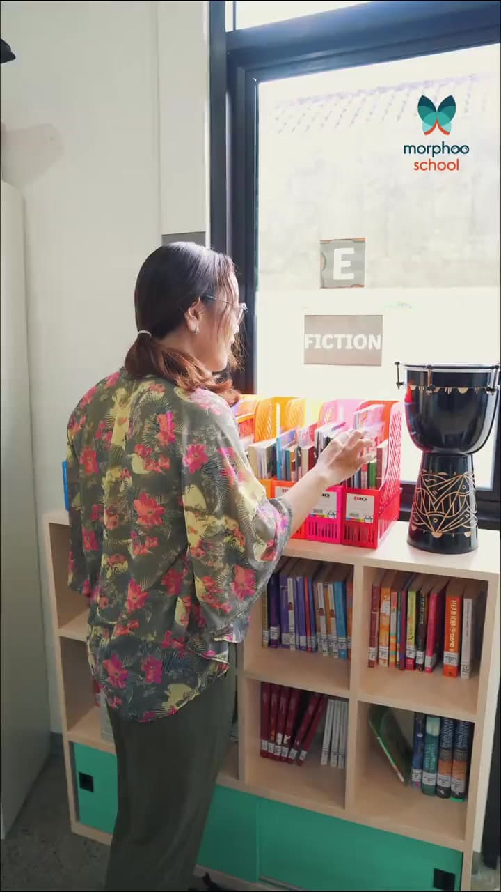 How My Students See Me?: Ms. Selvi, a Morphoo School teacher, in the school library, dressed in turn as a detective with a magnifying glass, a chef, a doctor, a hairdresser, a police officer, a judge and a clown, each with a pupil's line such as "Ms. Selvi, I lost my book!"